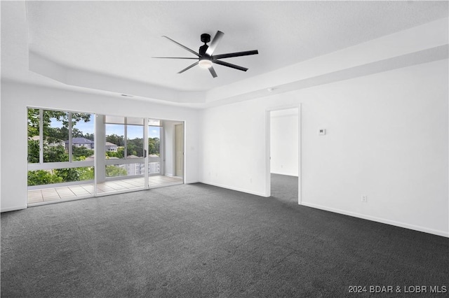 unfurnished room featuring dark colored carpet, ceiling fan, and a raised ceiling