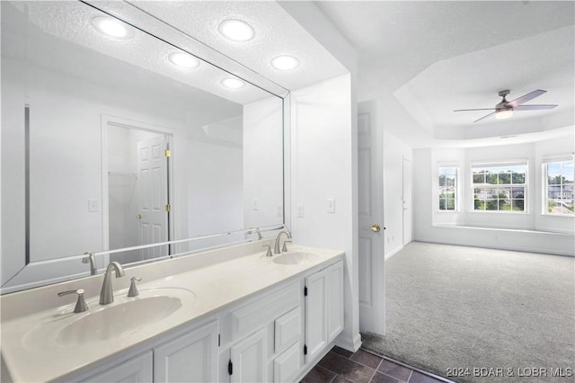 bathroom with ceiling fan, vanity, a raised ceiling, and a textured ceiling