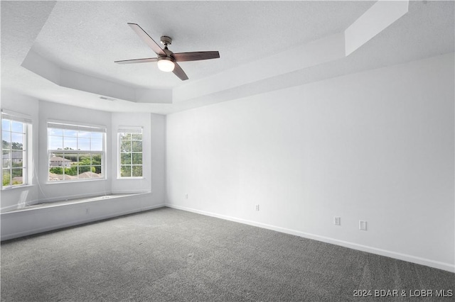 empty room with a tray ceiling, carpet flooring, a textured ceiling, and ceiling fan