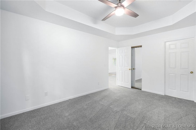 unfurnished bedroom featuring a tray ceiling, ceiling fan, carpet flooring, and a closet