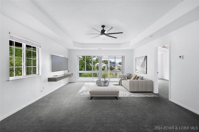 unfurnished living room featuring a tray ceiling, ceiling fan, dark carpet, and plenty of natural light