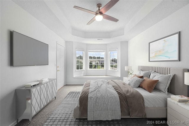 bedroom with ceiling fan, a raised ceiling, light carpet, and a textured ceiling