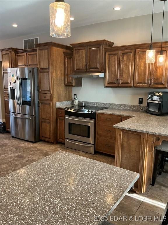 kitchen with light stone countertops, appliances with stainless steel finishes, decorative light fixtures, and a breakfast bar area