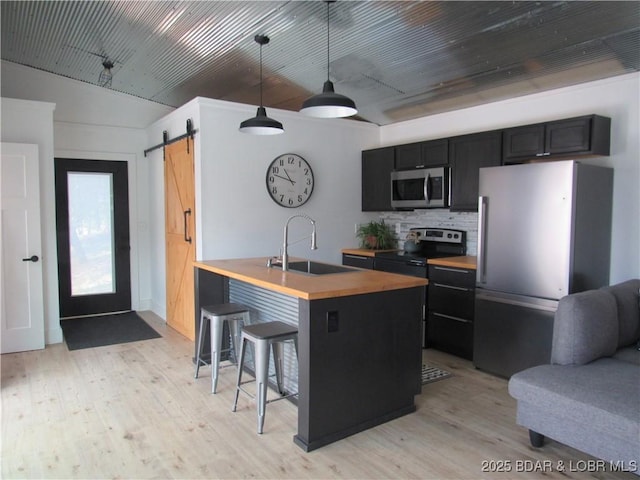 kitchen featuring a barn door, dark cabinets, stainless steel appliances, a sink, and wood counters