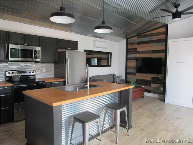 kitchen featuring wood counters, a breakfast bar, stainless steel appliances, light wood-style floors, and a sink