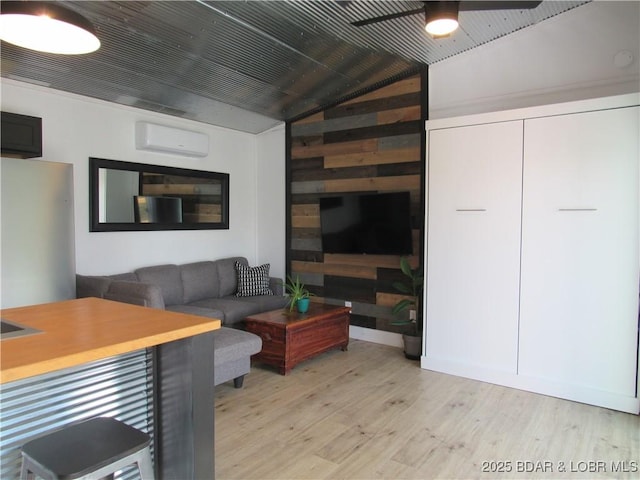 living area featuring vaulted ceiling, an AC wall unit, light wood-style flooring, and a ceiling fan