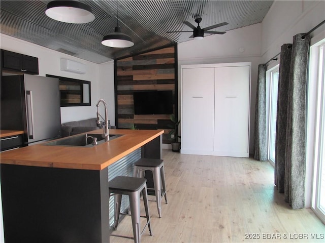 kitchen with wooden counters, light wood-style flooring, freestanding refrigerator, vaulted ceiling, and a sink