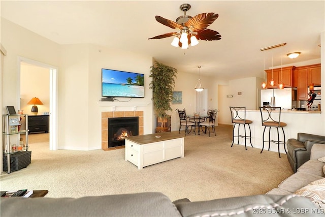 living area with a tiled fireplace, light colored carpet, and a ceiling fan