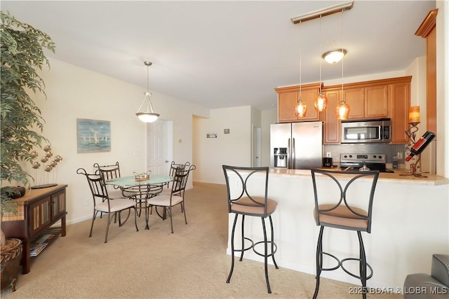 kitchen with a kitchen bar, light carpet, tasteful backsplash, stainless steel appliances, and a peninsula