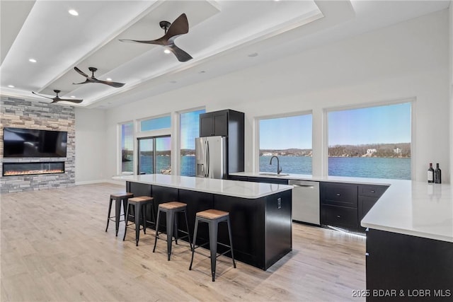 kitchen with light stone counters, light hardwood / wood-style floors, a kitchen bar, a water view, and appliances with stainless steel finishes