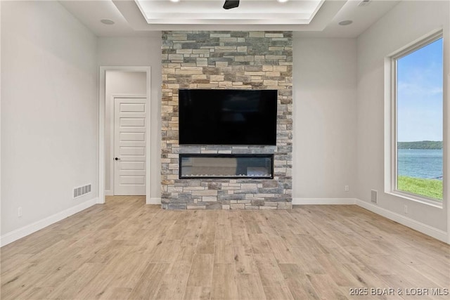 unfurnished living room with light hardwood / wood-style floors, a stone fireplace, and a tray ceiling