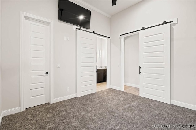 unfurnished bedroom with carpet, ensuite bathroom, ornamental molding, ceiling fan, and a barn door