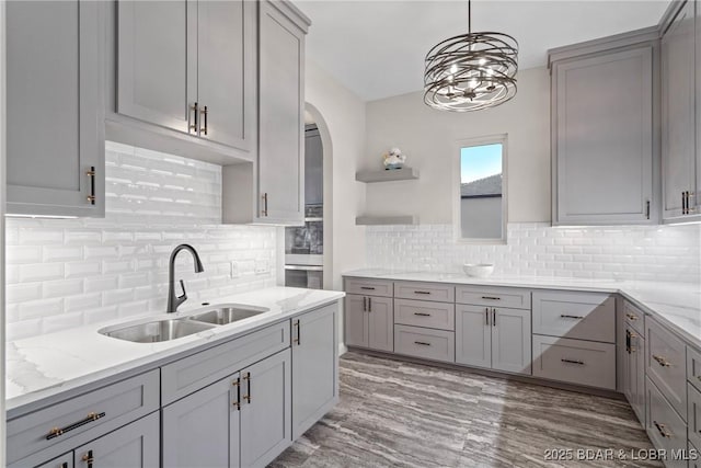 kitchen with gray cabinetry, light stone counters, and sink