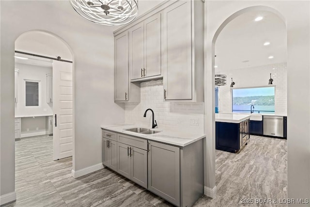 bar featuring dishwasher, gray cabinets, light stone counters, and sink