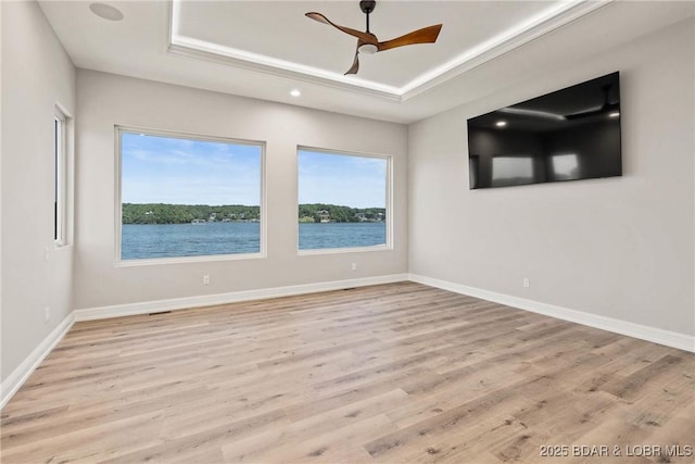 empty room featuring ceiling fan, light wood-type flooring, and a tray ceiling