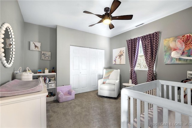 bedroom with a nursery area, ceiling fan, carpet flooring, and a closet