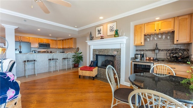 living room with a high end fireplace, light hardwood / wood-style flooring, ceiling fan, and ornamental molding