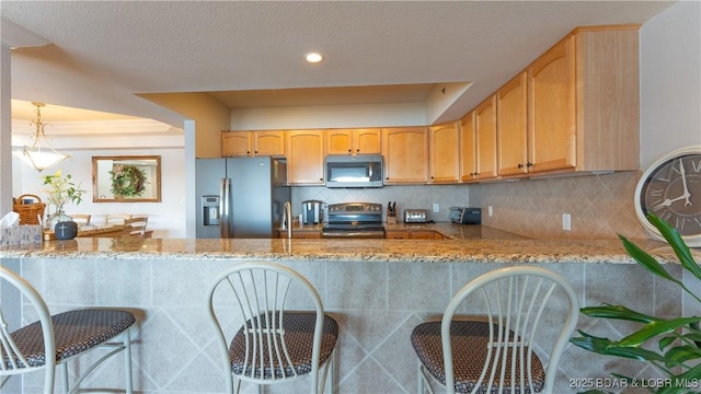 kitchen with kitchen peninsula, appliances with stainless steel finishes, backsplash, and light stone counters