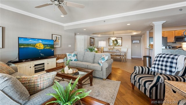 living room featuring a raised ceiling, light hardwood / wood-style flooring, ceiling fan, ornate columns, and ornamental molding