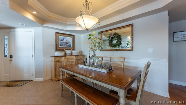 dining space with light tile patterned floors, a raised ceiling, and ornamental molding