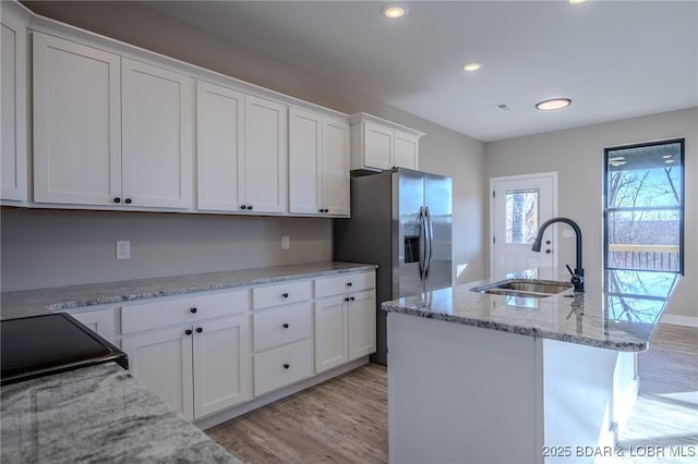 kitchen featuring light stone counters, a center island with sink, white cabinetry, and sink