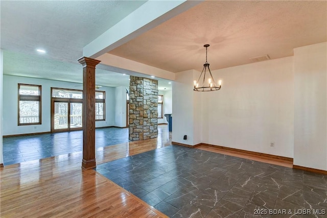 empty room featuring a textured ceiling, decorative columns, and a notable chandelier