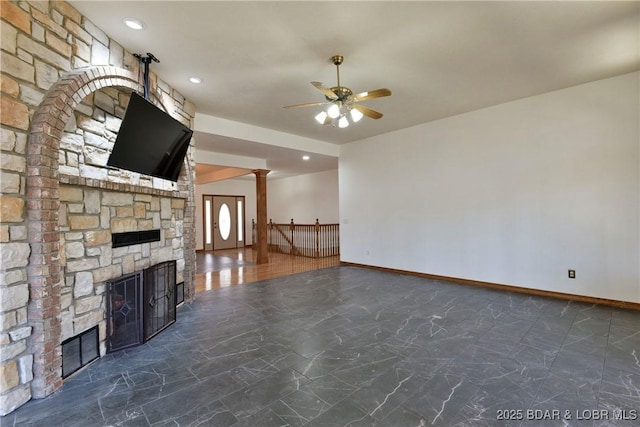 unfurnished living room with a stone fireplace, ceiling fan, and ornate columns