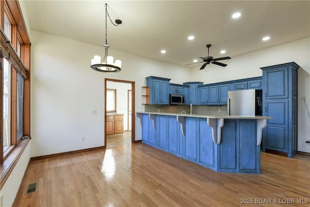 kitchen featuring backsplash, blue cabinets, hanging light fixtures, appliances with stainless steel finishes, and a breakfast bar area