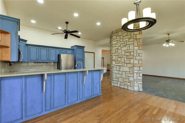 kitchen featuring dark wood-type flooring, stainless steel appliances, a kitchen breakfast bar, blue cabinets, and backsplash