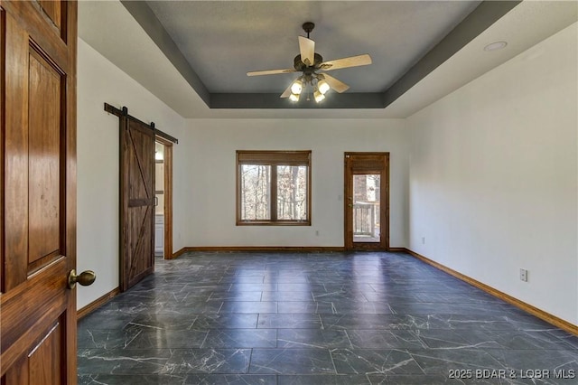 spare room with a barn door, a tray ceiling, and ceiling fan