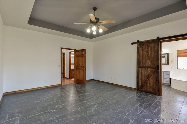 unfurnished room with a tray ceiling, a barn door, and ceiling fan