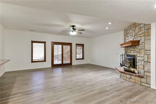 unfurnished living room featuring a wood stove, ceiling fan, a textured ceiling, and light wood-type flooring