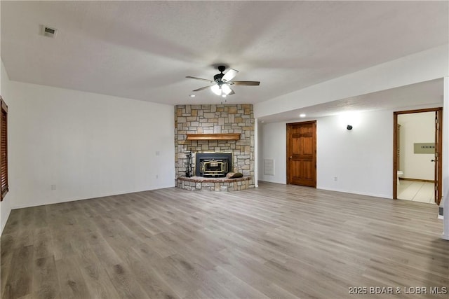 unfurnished living room with a wood stove, ceiling fan, light hardwood / wood-style flooring, and a textured ceiling