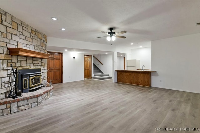 unfurnished living room with a wood stove, ceiling fan, light hardwood / wood-style flooring, and sink