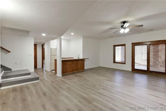 unfurnished living room with ceiling fan, a textured ceiling, and light wood-type flooring