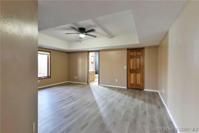 unfurnished room featuring ceiling fan, light hardwood / wood-style floors, a raised ceiling, and a textured ceiling