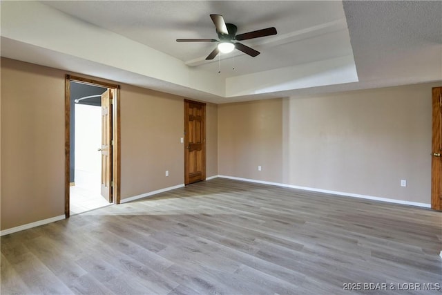 spare room featuring a tray ceiling, light hardwood / wood-style flooring, and ceiling fan