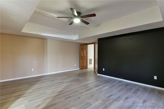 unfurnished room with a textured ceiling, a tray ceiling, hardwood / wood-style flooring, and ceiling fan