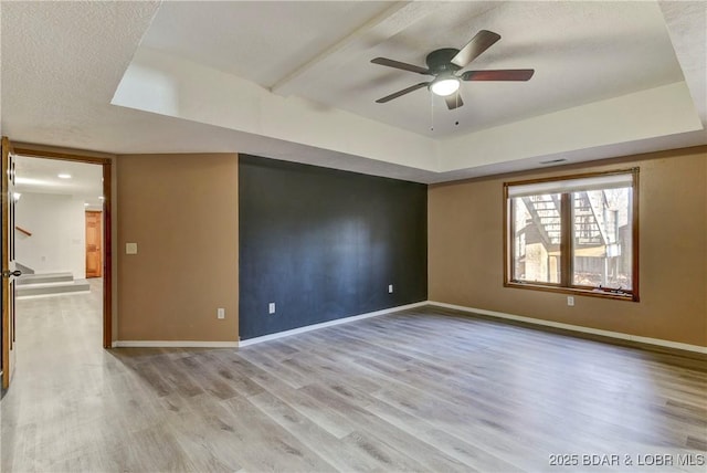 unfurnished room featuring ceiling fan, a textured ceiling, a tray ceiling, and light hardwood / wood-style flooring