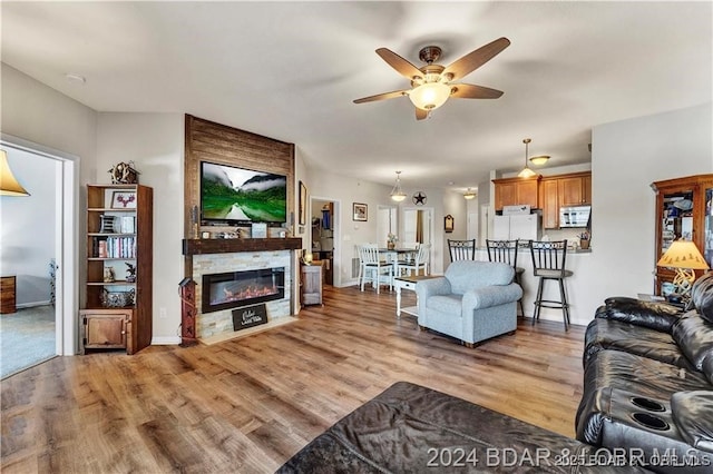 living room featuring ceiling fan, a large fireplace, and light wood-type flooring