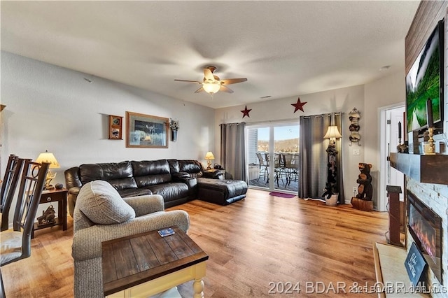 living room with a ceiling fan, a fireplace with flush hearth, and light wood finished floors