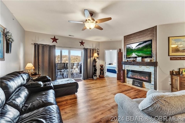 living room with wood-type flooring, a stone fireplace, and ceiling fan