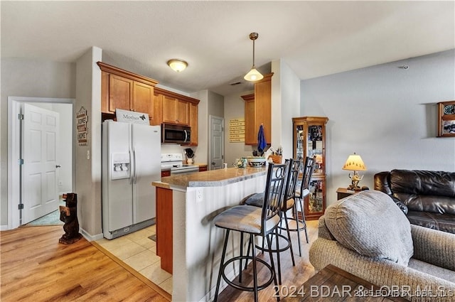 kitchen with a breakfast bar, light tile patterned flooring, white appliances, and kitchen peninsula