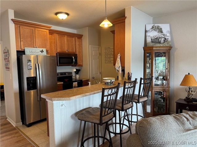 kitchen with appliances with stainless steel finishes, light countertops, brown cabinets, a kitchen breakfast bar, and a peninsula