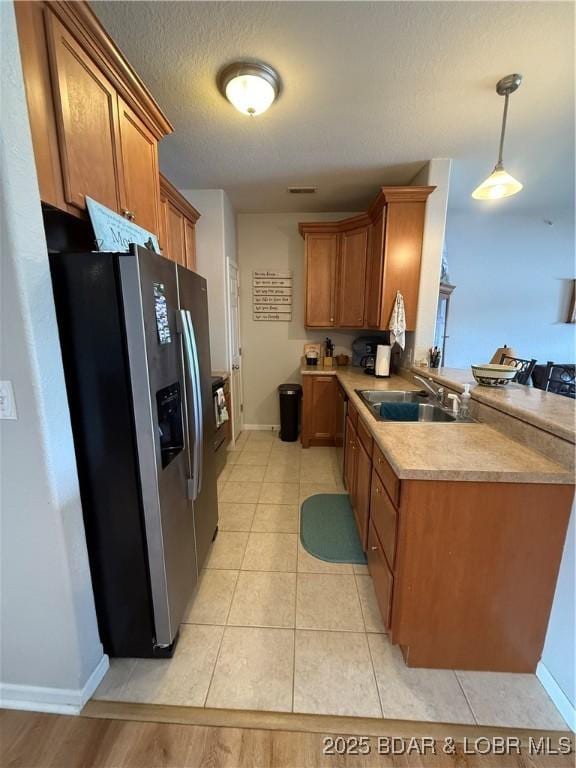 kitchen featuring stainless steel refrigerator with ice dispenser, a sink, brown cabinetry, baseboards, and a peninsula
