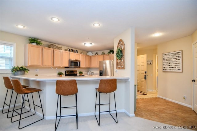 kitchen featuring a kitchen breakfast bar, light brown cabinets, kitchen peninsula, and stainless steel appliances