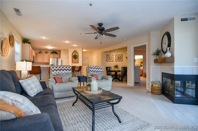 living room featuring a fireplace, light carpet, and ceiling fan