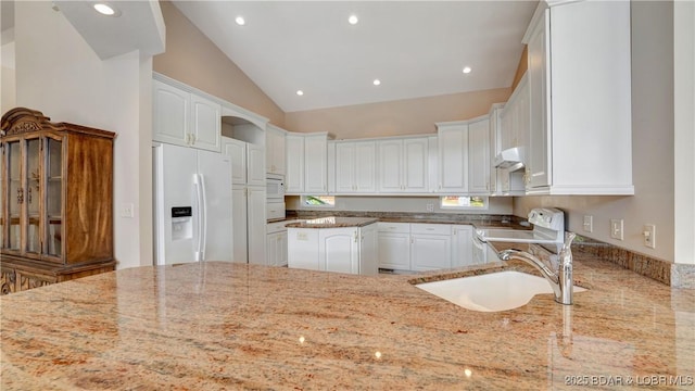 kitchen with light stone counters, white appliances, sink, white cabinetry, and lofted ceiling