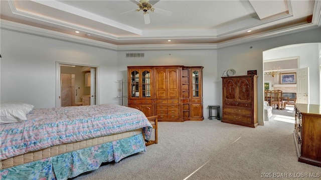 bedroom featuring ceiling fan, light carpet, connected bathroom, and a tray ceiling