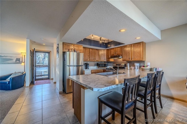 kitchen featuring sink, a kitchen breakfast bar, kitchen peninsula, a textured ceiling, and appliances with stainless steel finishes